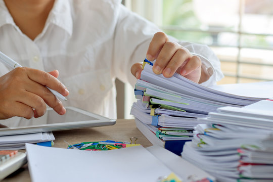 Teacher hand is searching student report and homework assignment on desk in school for score. Unfinished paperwork stacked in archive with color papers and paper clips. Education and business concept.