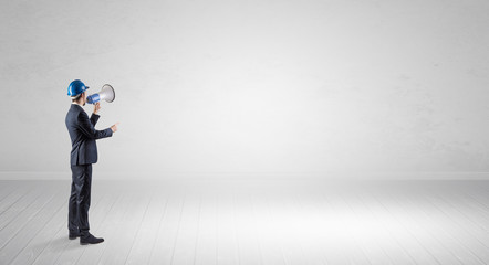 Young architect with construction helmet standing in an empty space and holding a plan
