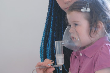 Girl inhaling through inhaler mask with her mom. Use nebulizer and inhaler for the treatment.