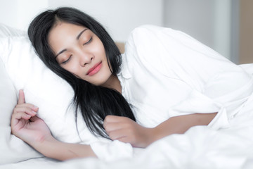 Obraz na płótnie Canvas Beautiful young pretty Asian woman wake up and make happy smile with white shirt at the white bed in the morning. 
