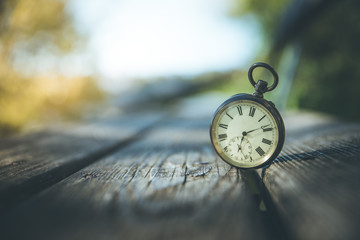 Retro Taschenuhr auf Holzbank, Himmel und bunte Blätter im Herbstlicht, Symbol für Zeit