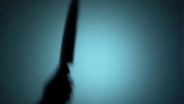 Killer slashing victim with a knife, spooky silhouette behind the glass, murder. Blood-chilling horror thriller shot