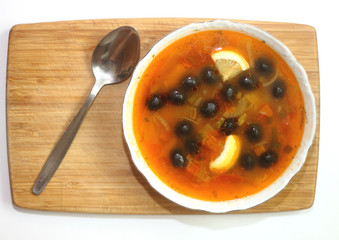 kitchen delicious Solyanka soup with olives meat and lemon in a round plate with a spoon on a wooden chopping Board