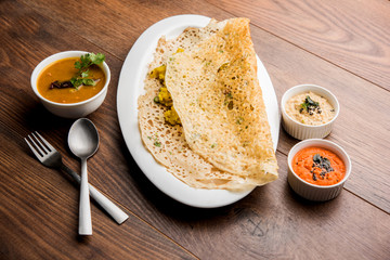 Onion rava masala dosa is a South Indian instant breakfast served with chutney and sambar over moody background. selective focus
