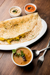 Onion rava masala dosa is a South Indian instant breakfast served with chutney and sambar over moody background. selective focus