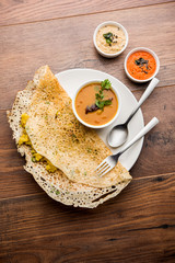 Onion rava masala dosa is a South Indian instant breakfast served with chutney and sambar over moody background. selective focus