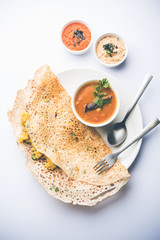 Onion rava masala dosa is a South Indian instant breakfast served with chutney and sambar over moody background. selective focus
