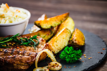 Grilled steak with baked potatoes and vegetables served on black stone on wooden table