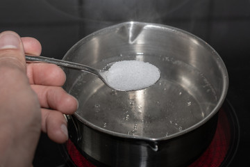 Löffel in der Hand und Salz in das kochende Wasser in der Pfanne schütten