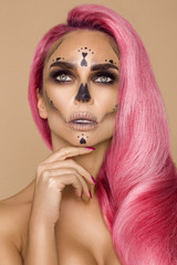 Beautiful blonde woman in Halloween makeup and in pink hair on a beige background in the studio....