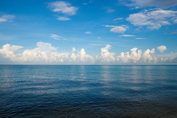 Infinite horizon with puffy white tropical clouds above calm blue empty sea
