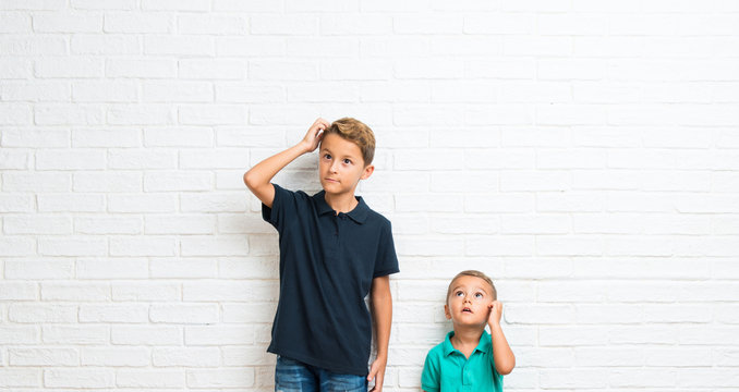 Two little brothers having doubts and with confuse face expression while scratching head