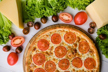 Italian hot pizza surrounded by fresh ingredients on light wooden background