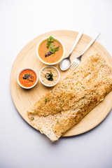Onion rava masala dosa is a South Indian instant breakfast served with chutney and sambar over moody background. selective focus