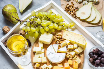 Different types of cheese on wooden board, olive, fruits, almond and wine glasses on white tray © voloshin311