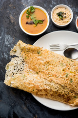 Onion rava masala dosa is a South Indian instant breakfast served with chutney and sambar over moody background. selective focus