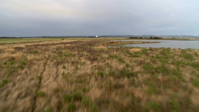 Aerial Shot very low skimming over marsh land flying towards a cargo ship the Celtic Navigator ( IMO 9003548 ) on the Humber river.