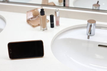 洗面台でメイクをする　リキッドファンデーション、リップスティック、スマートフォン