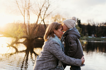 Mother and child hugging at autumn park near the lake. Happy son with mom having fun, relaxing, enjoying life. Mothers's day, family waking on park.