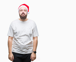 Naklejka premium Young caucasian hipster man wearing christmas hat over isolated background with serious expression on face. Simple and natural looking at the camera.