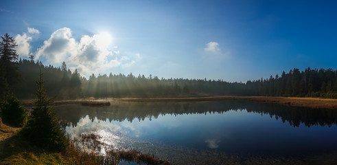 Autumn morning at lake, sun rays glowing through mist