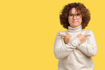Beautiful middle ager senior woman wearing turtleneck sweater and glasses over isolated background Pointing to both sides with fingers, different direction disagree