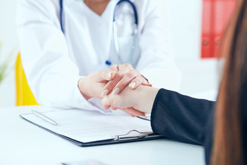 Friendly female doctor's hands holding female patient's hand for encouragement and empathy close-up. Partnership, trust and medical ethics concept.