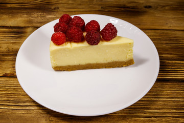 Piece of tasty New York cheesecake with raspberries in a white plate on wooden table