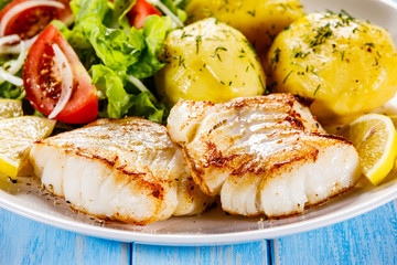 Fried fish with potatoes on wooden table