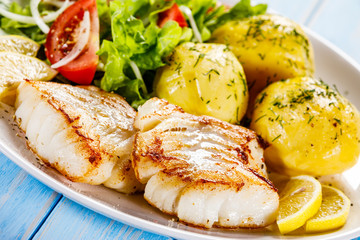 Fried fish with potatoes on wooden table