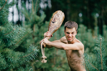Odd primitive naked man with huge wooden stick hunting in forest. Adult male have fun like crazy...