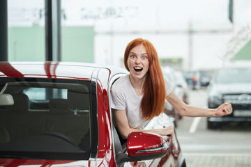 Car sale, consumerism and human emotions concept. Emotionally colored photo of overjoyed woman half sticking out from a car window screaming at camera, feeling herself the happiest woman at the world