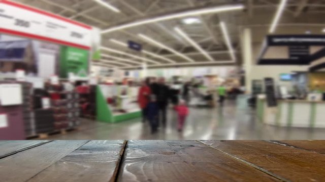 Defocused image of a crowd of buyers. People walk around the building store. A wooden table or counter in the foreground.