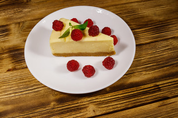 Piece of tasty New York cheesecake with raspberries in a white plate on wooden table