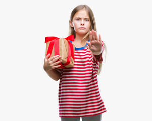 Young beautiful girl giving christmas or valentine gift over isolated background with open hand doing stop sign with serious and confident expression, defense gesture