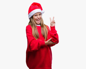 Young beautiful girl wearing christmas hat over isolated background smiling with happy face winking at the camera doing victory sign. Number two.