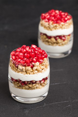 Pomegranate parfait - sweet organic layered dessert with granola flakes, yogurt and fruit seeds on black background.