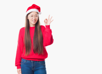 Young Chinese woman over isolated background wearing christmas hat smiling positive doing ok sign with hand and fingers. Successful expression.