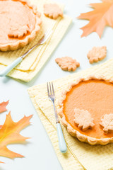 Pumpkin pie with cinnamon and cookies on yellow napkins on pastel blue background with autumn yellow leaves.