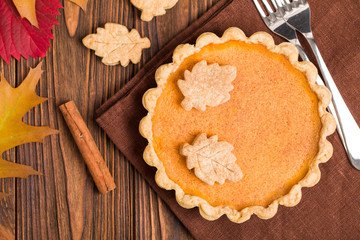 Obraz na płótnie Canvas Pumpkin pie with cinnamon and cookies on brown napkins on wooden background with autumn yellow leaves.