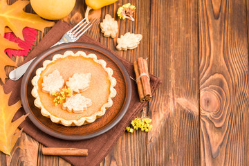 Pumpkin pie with cinnamon and cookies on brown napkins on wooden background with autumn yellow leaves.