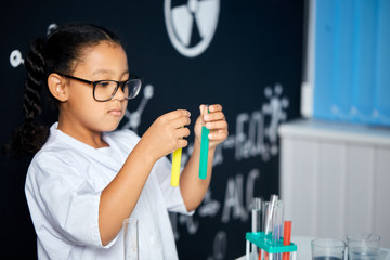 Cute female Vietnamese pupil in protective glasses and white uniform, doing biochemistry research in chemistry class