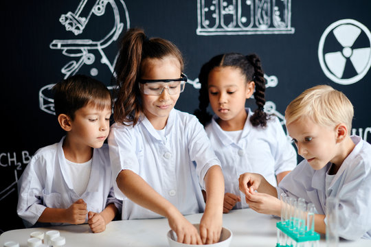 Multiethnic group of 7 years old kids in white lab coats doing a chemical experiment in laboratory at school.
