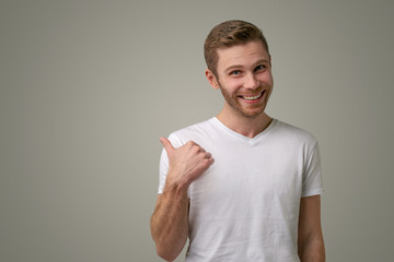 An unshaven man with blue eyes points his thumb at the copy space. A handsome guy shows something...