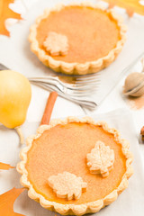 Pumpkin pie with cinnamon and cookies on gray napkins on white wooden background with autumn yellow leaves.