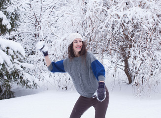 Young pretty woman playing snowball fight in a winter forest.