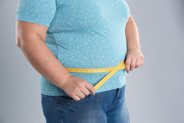 Overweight woman measuring waist before weight loss on color background