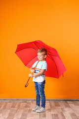 Little boy with red umbrella near color wall