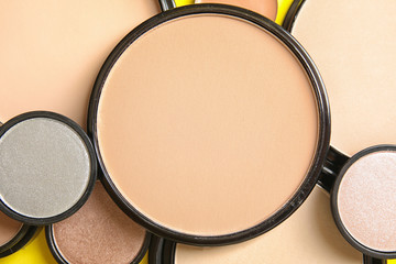 Various shades of face powder and other makeup products as background, closeup
