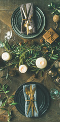 Christmas or New Years celebration party table setting. Flat-lay of plates, golden cutlery, glasses, festive branch decoration, candles and gliterring toys over wooden table background, top view